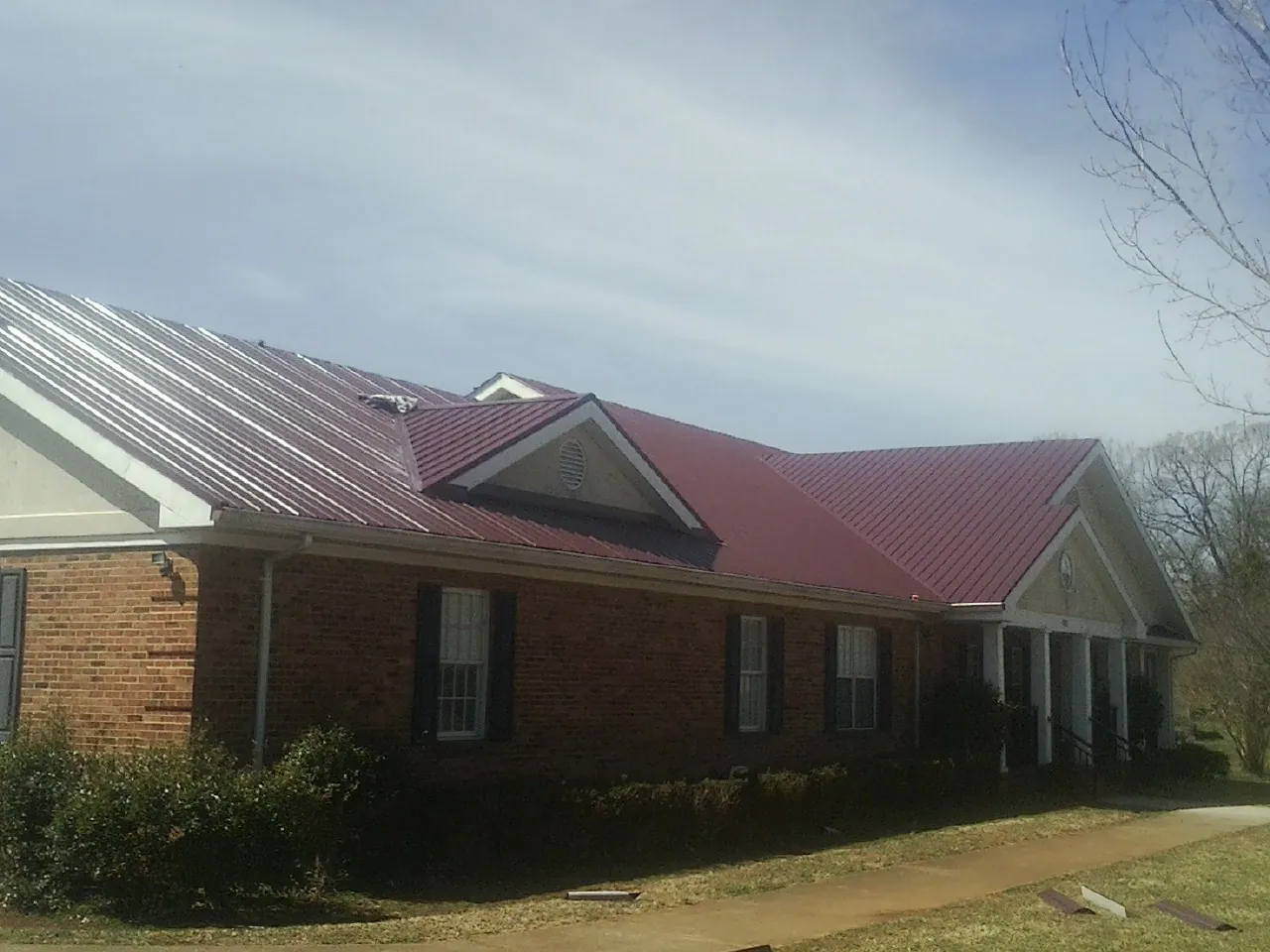 Red metal roof with gabled entries on a long brick building, from a Hail Damage Roof Repair job in Greenhurst