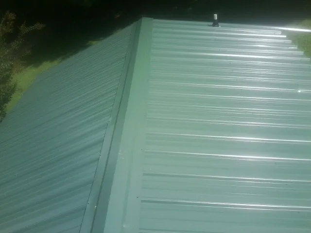 New green metal panels meeting at the ridge of a roof — Flat Roof Repair work by our crew in Greenhurst