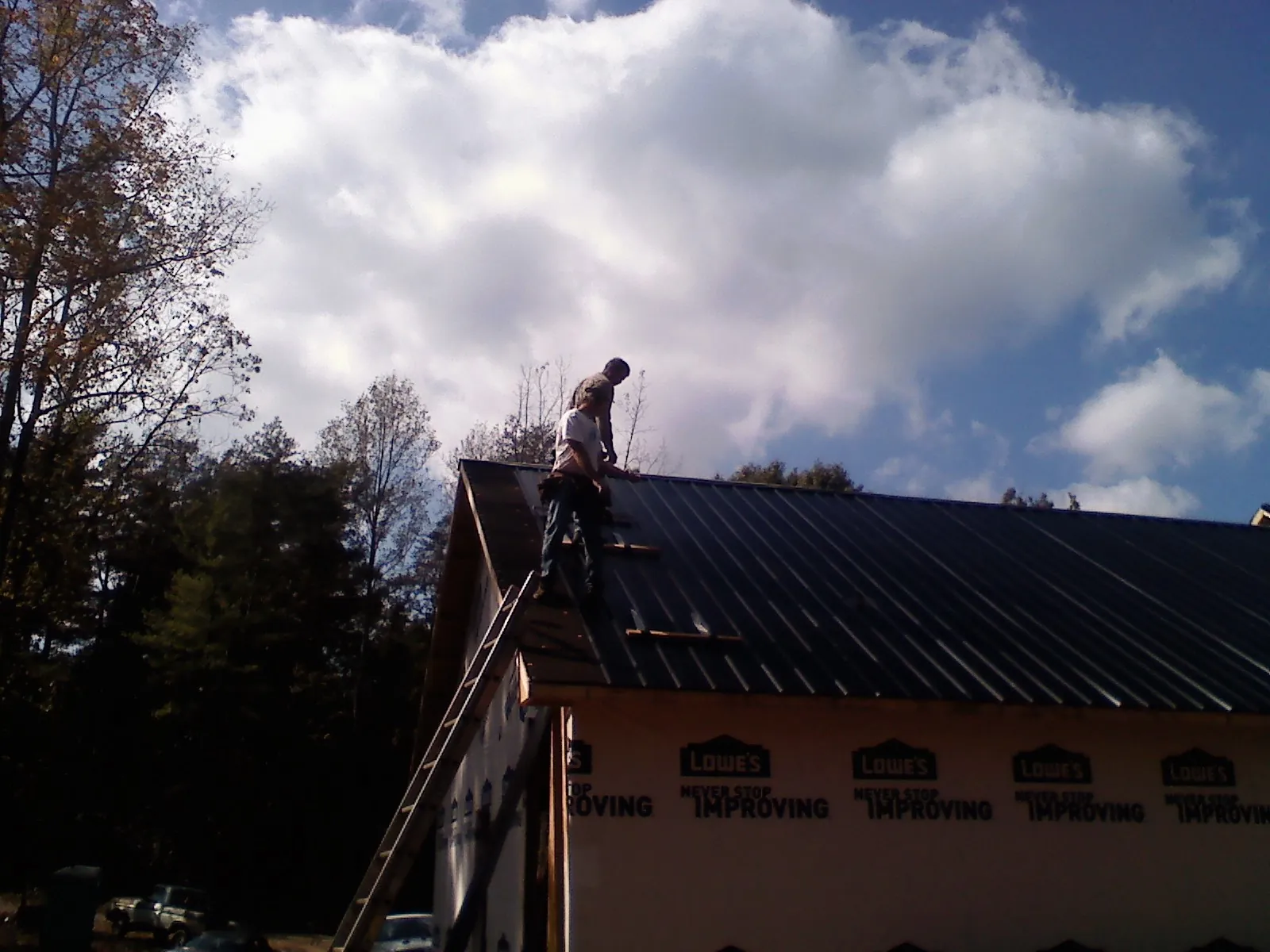 Roofer fastening dark metal panels high against a cloudy sky, from a Roof Inspection job in Greenhurst