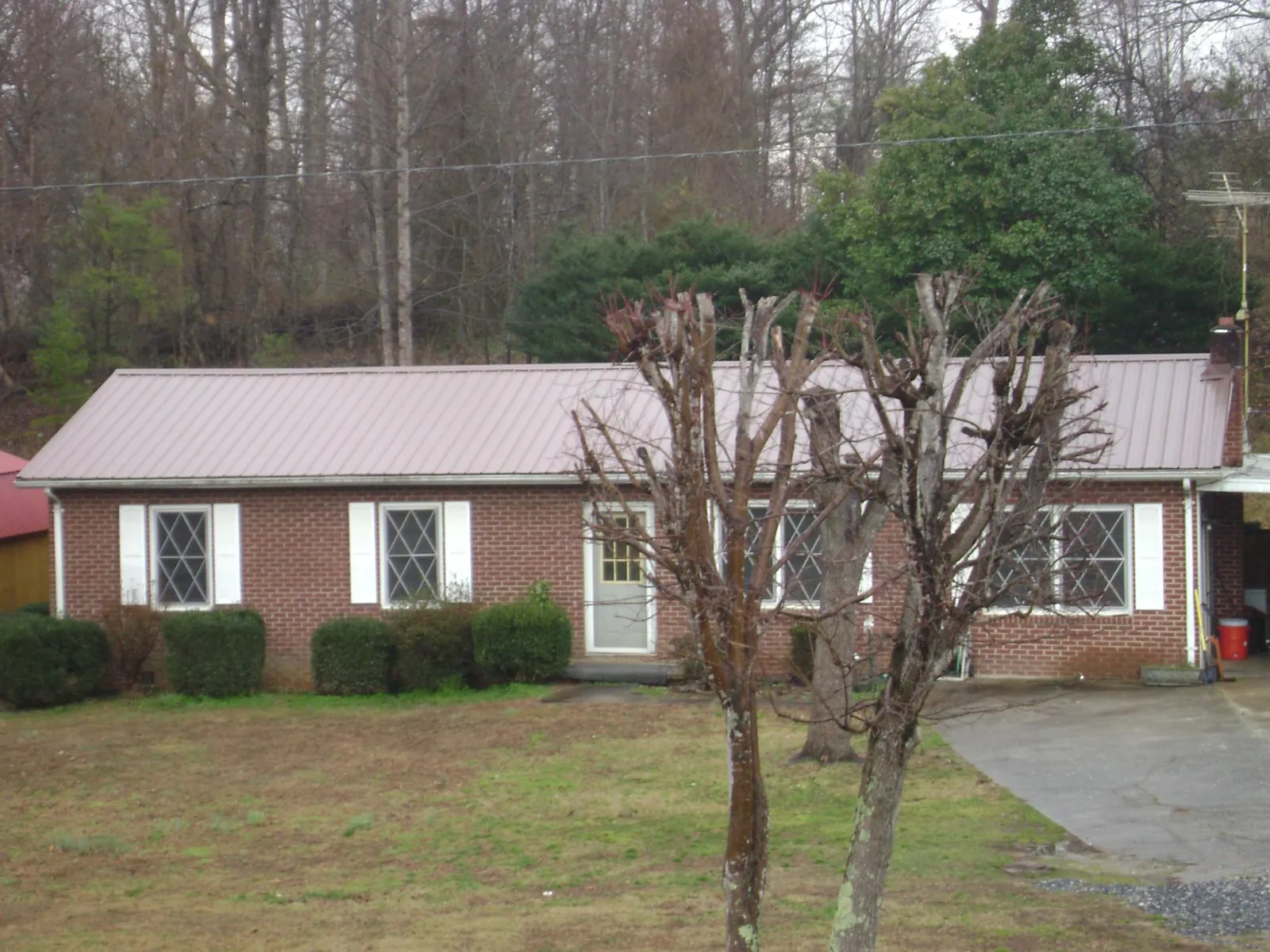 Mauve metal roof on a brick ranch home behind bare trees in Greenhurst