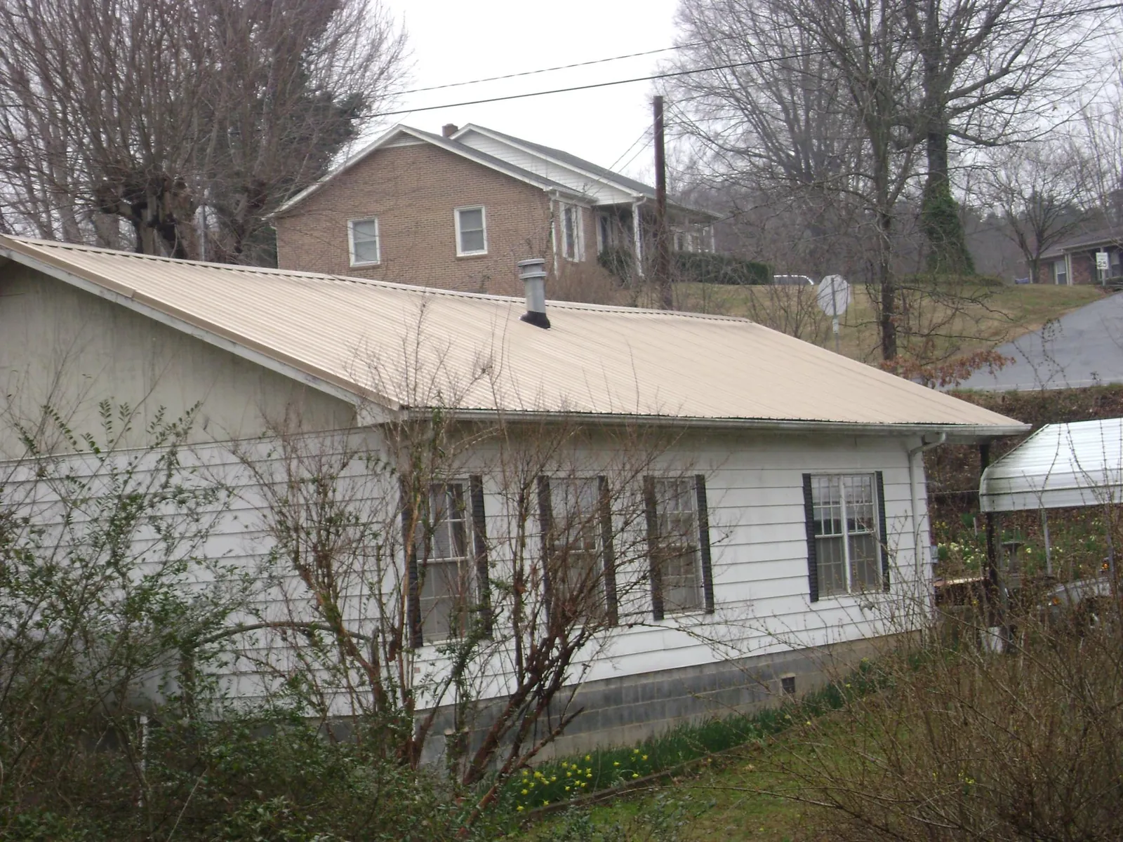 Tan metal roof on a white sided house set into a hillside — Commercial Roofing by Roofing Brothers in Greenhurst