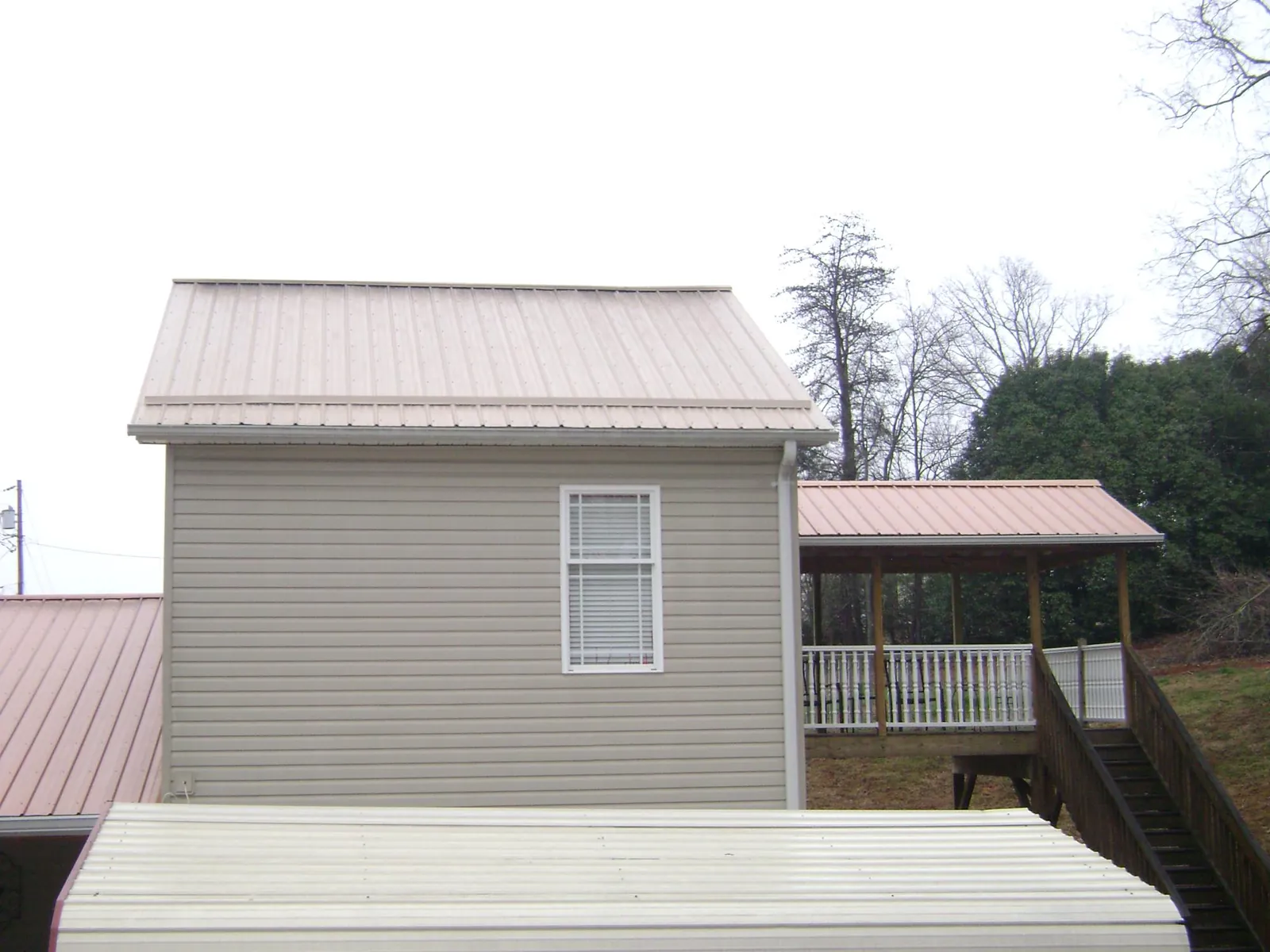 Tan metal roofs on a two story addition and attached porch, from a Roof Replacement job in Greenhurst